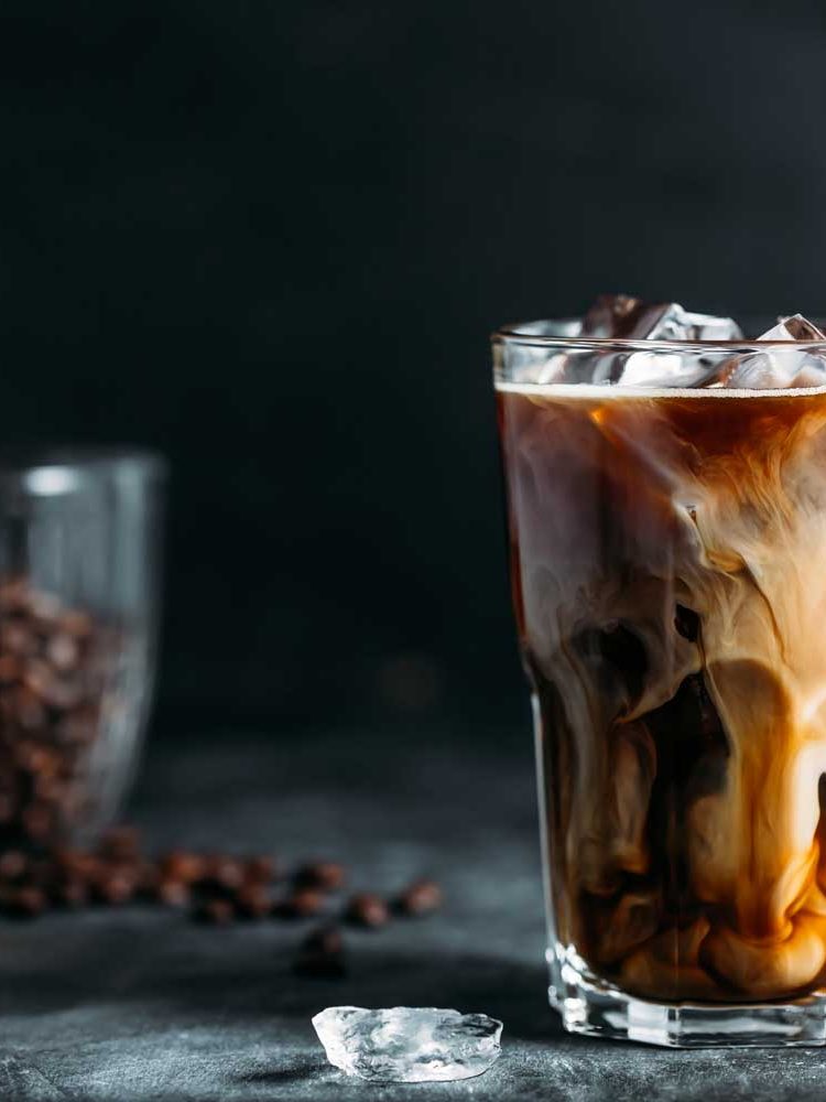 milk-being-poured-into-iced-coffee-on-a-dark-table-TH2MABV.jpg